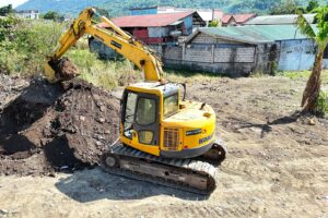 A Komatsu excavator loading soil on an active job site with hills in the background