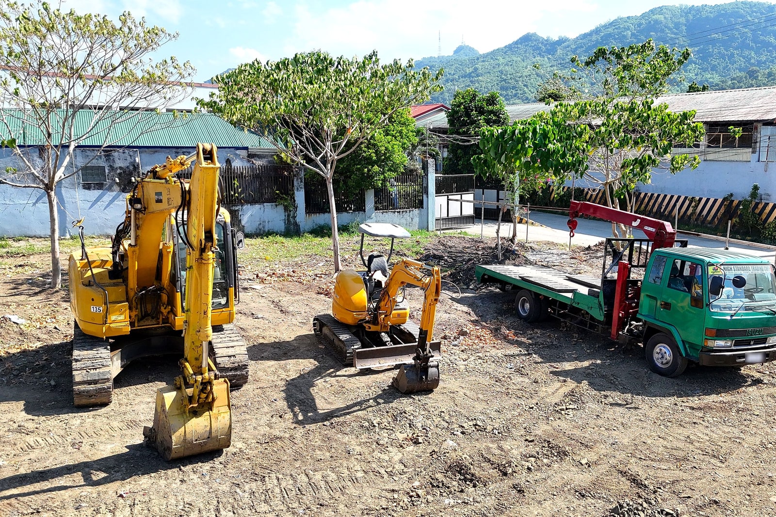 Two excavators and a flatbed crane truck staged on site with mountains in the background