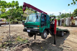 A green boom truck with crane arm extended at a job site