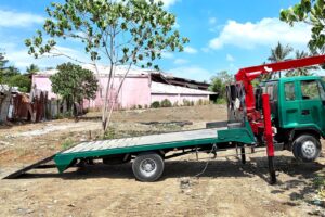 A flatbed truck with its loading ramp lowered, ready to receive equipment
