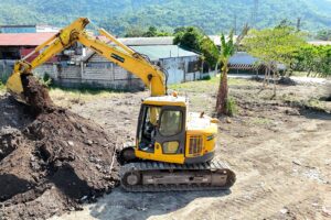 A Komatsu excavator digging soil on a job site with hills in the background