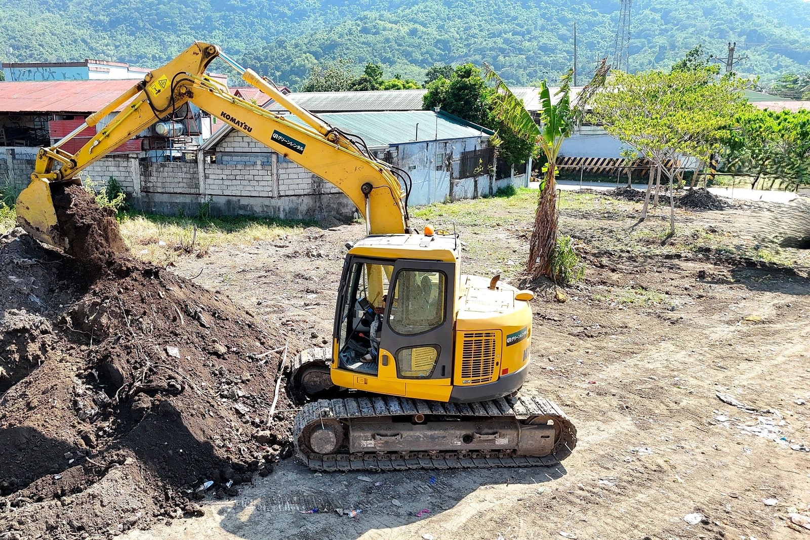 A Komatsu excavator digging soil on a job site with hills in the background