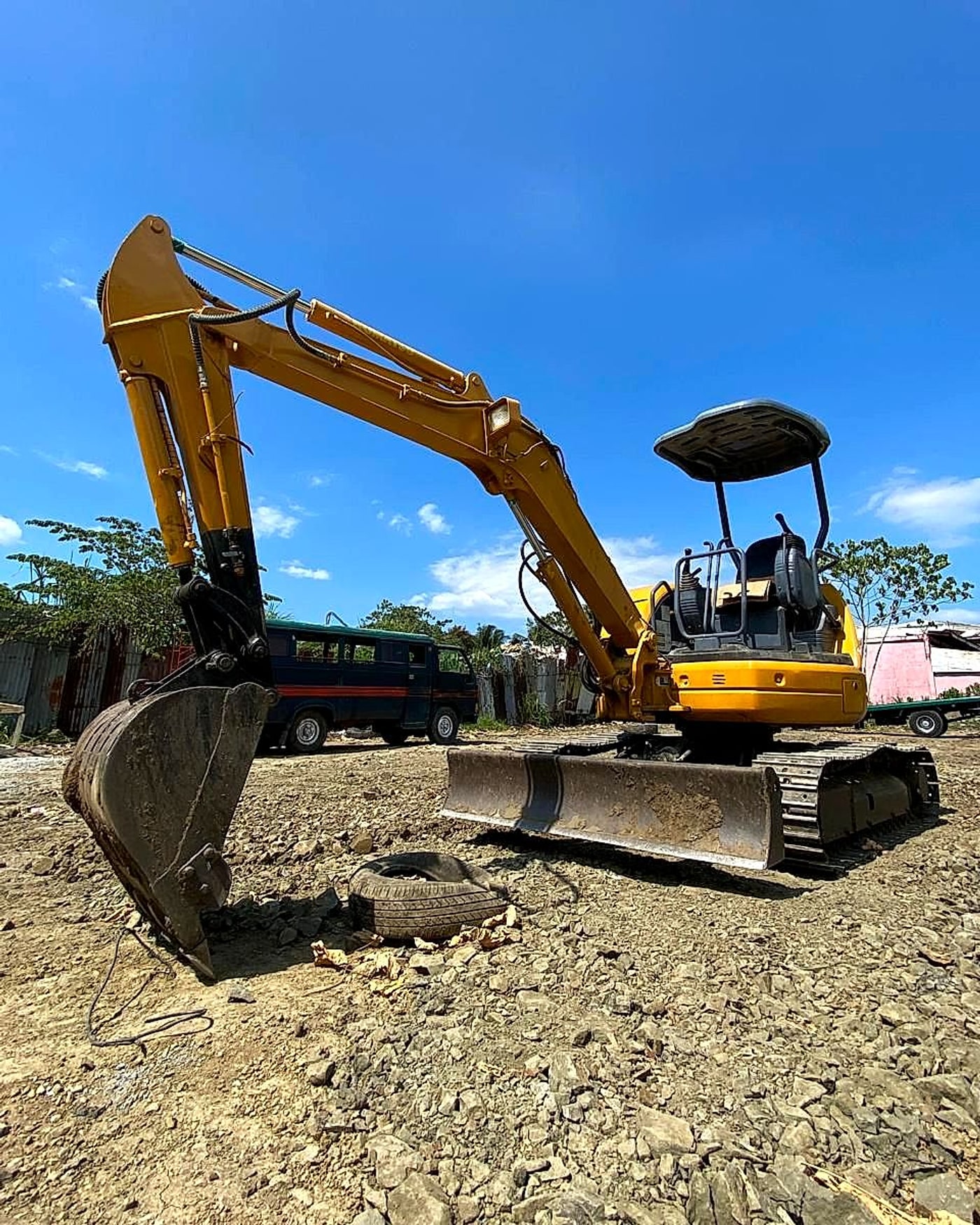 Low-angle view of a mini excavator bucket and boom against a bright blue sky