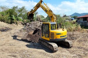 Side profile of a yellow Komatsu excavator mid-dig, with hills in the background