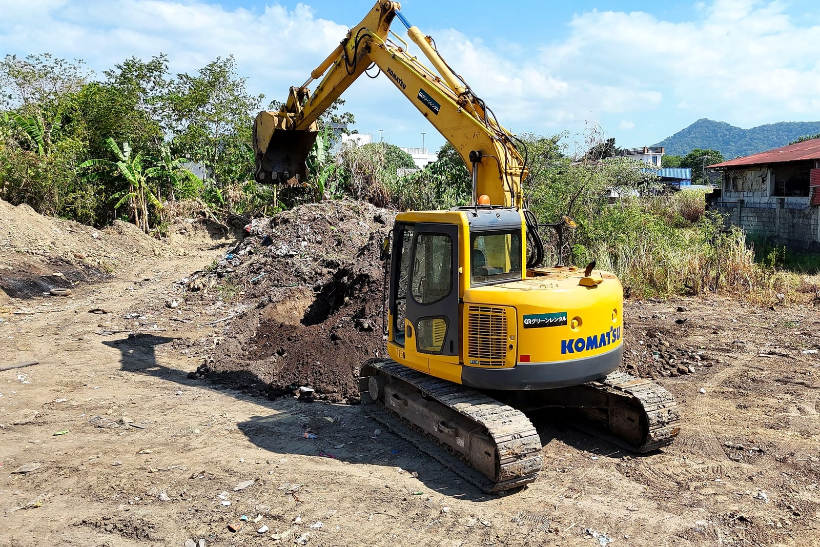 Side profile of a yellow Komatsu excavator mid-dig, with hills in the background