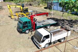 An excavator and two flatbed trucks staged at a job site, aerial view