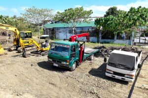 Two excavators and two flatbed trucks staged on a Philippine job site
