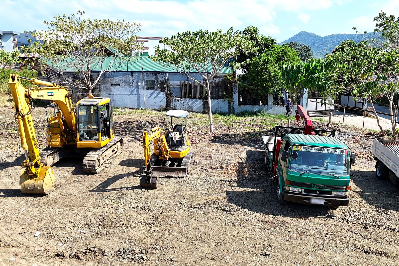 An excavator, mini excavator, and flatbed crane truck staged at a job site with hills in the background